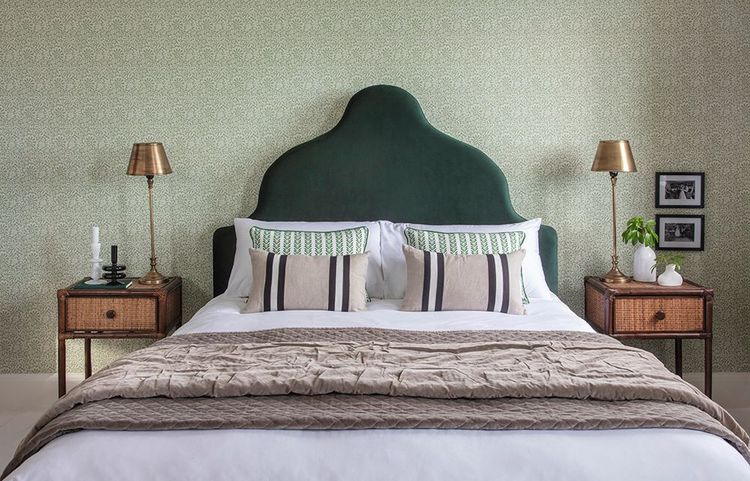 Cozy bedroom with a green headboard, patterned pillows, and a beige quilt. Two bedside tables with lamps and framed photos complete the decor.