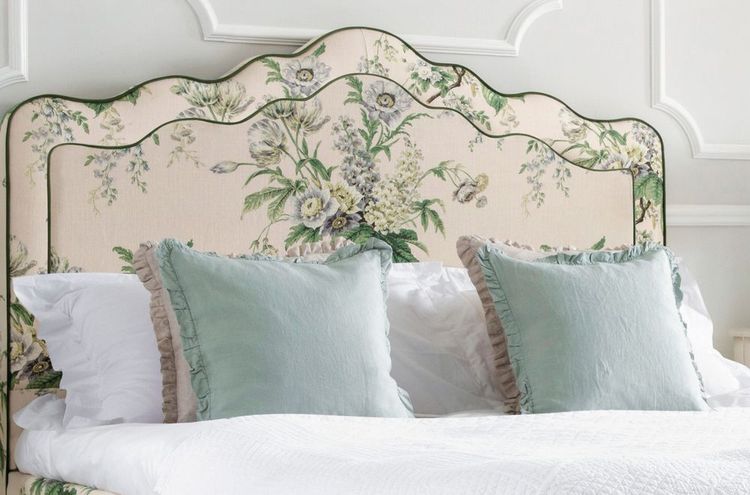 Elegant bed with a floral-patterned headboard, adorned with two light blue, ruffled pillows and white bedding in a softly lit room.
