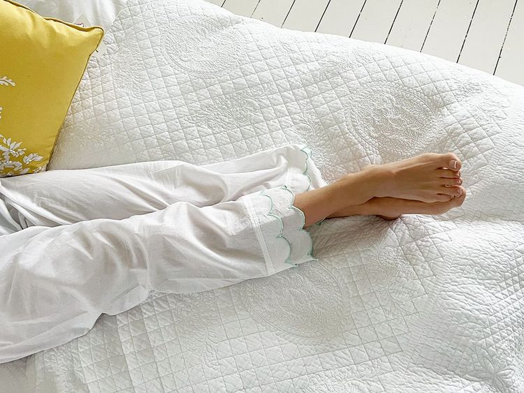 Person in white pajamas lying on a quilted bed with a yellow pillow, feet crossed and relaxed.