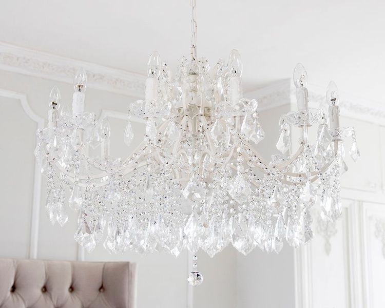 Elegant crystal chandelier with ornate detailing and multiple candle-shaped bulbs, hanging in a bright, white room with decorative molding.
