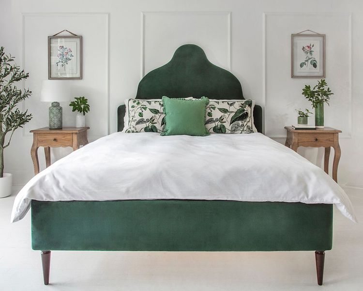Elegant bedroom with a green upholstered bed, white bedding, wooden side tables, and botanical wall art, creating a fresh and serene atmosphere.