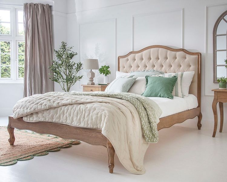 Elegant bedroom with a tufted headboard bed, green and beige bedding, wooden furniture, potted plant, and large window with curtains.