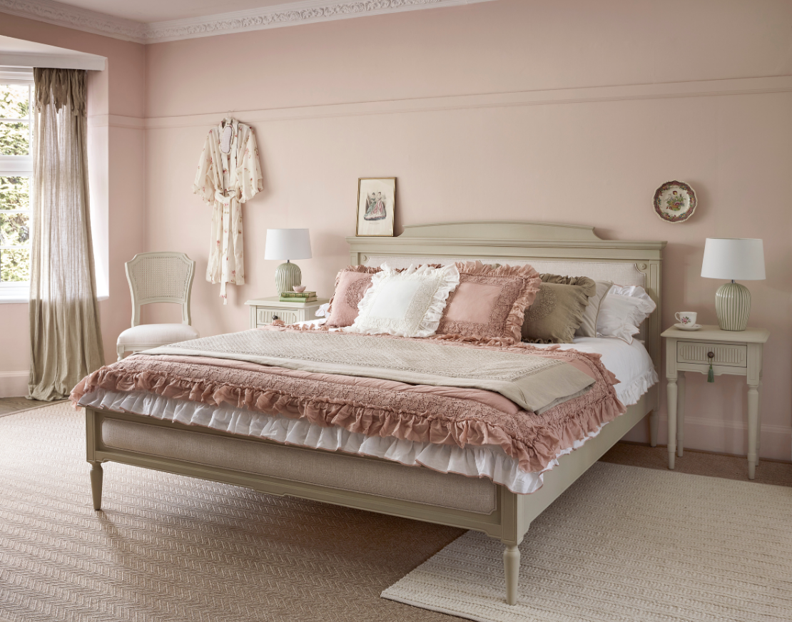 Elegant bedroom with a pink and beige theme, featuring a large bed with layered bedding, matching nightstands, decorative lamps, and a soft rug.