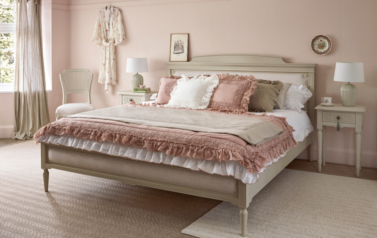 Elegant bedroom with a pink and beige theme, featuring a large bed with layered bedding, matching nightstands, decorative lamps, and a soft rug.