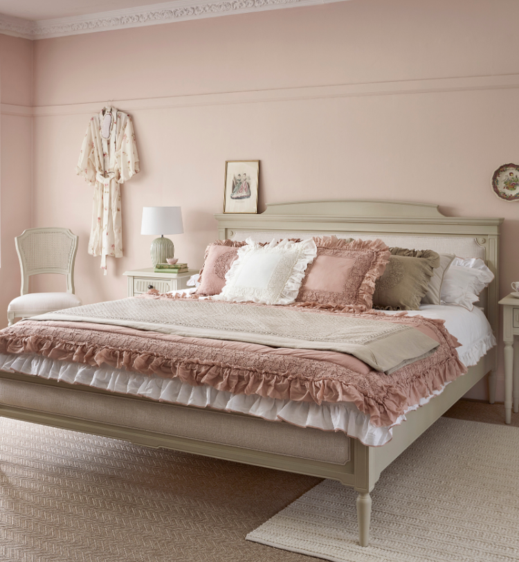 Elegant bedroom with a pink and beige theme, featuring a large bed with layered bedding, matching nightstands, decorative lamps, and a soft rug.