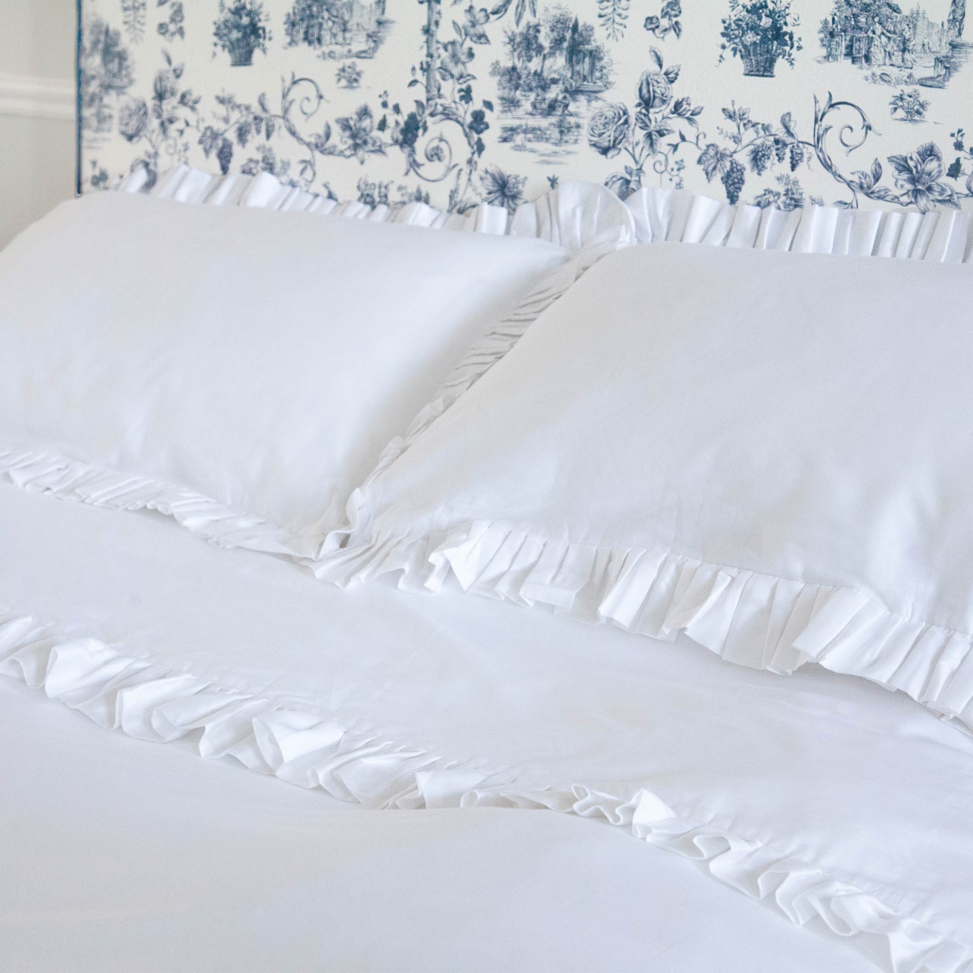 A neatly made bed with white ruffled pillows and sheets, set against a blue and white patterned headboard.