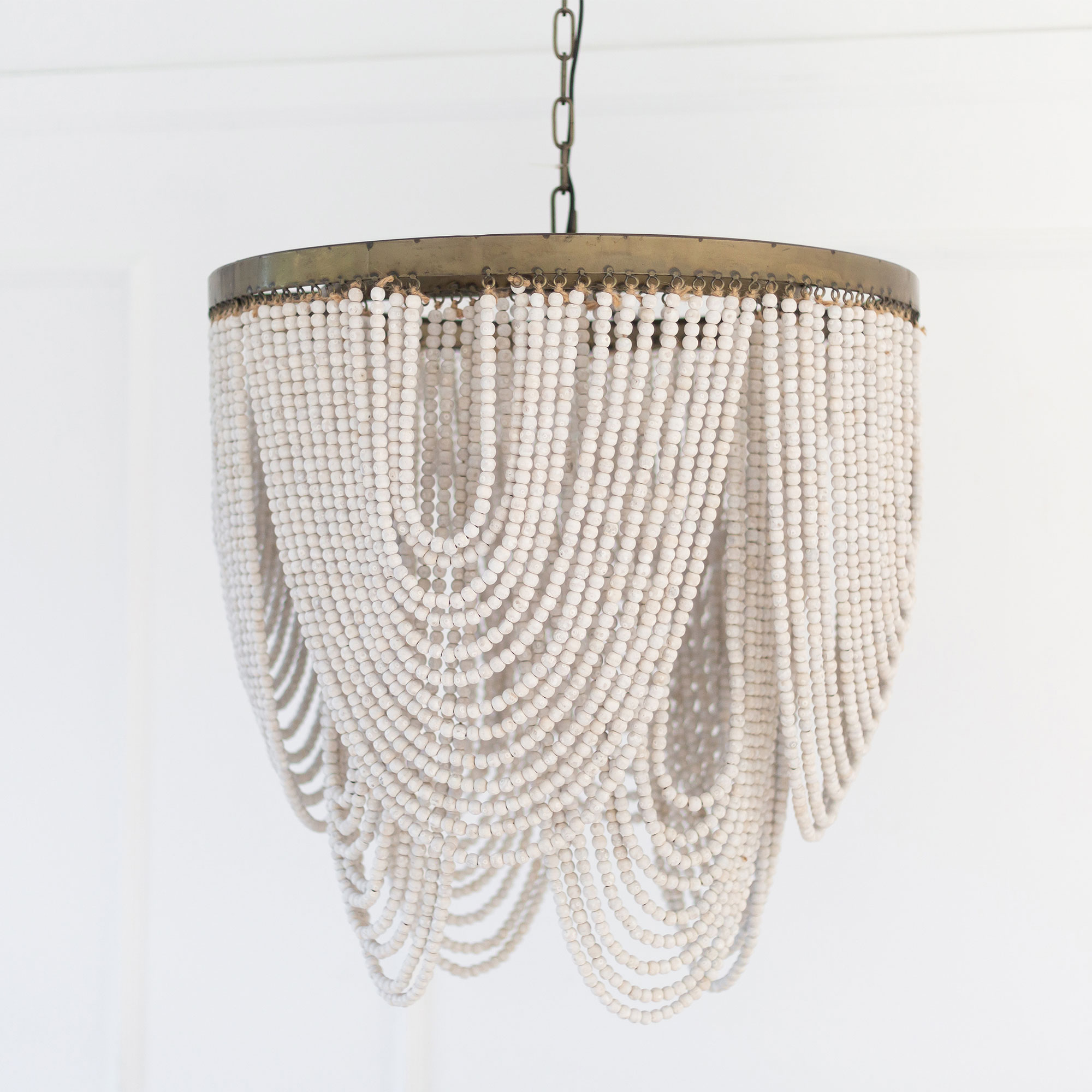 A hanging chandelier with cascading strands of white beads and a bronze rim, set against a white background.