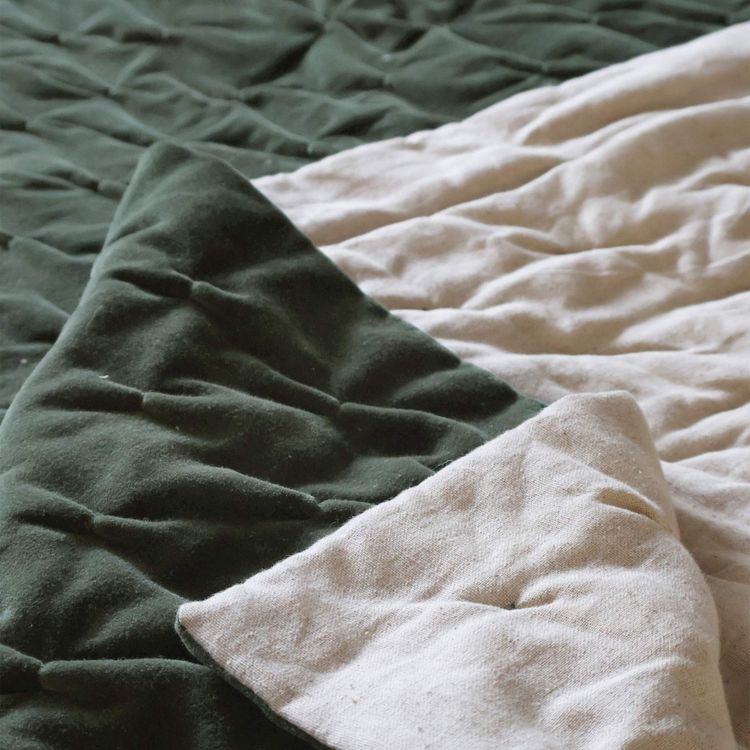 Close-up of a soft, quilted bedspread in dark green and beige, showing textured folds and stitching details.