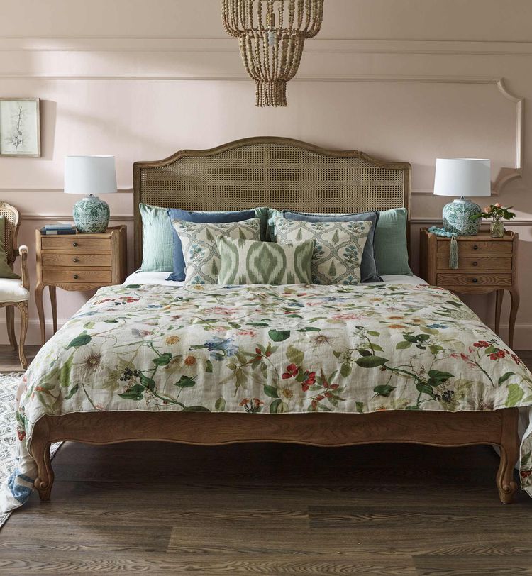 Elegant bedroom with a wooden rattan bed, floral bedspread, blue and green pillows, and bedside tables with lamps.