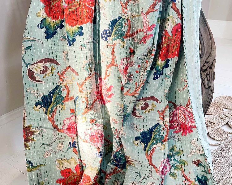 Close-up of a vibrant quilt with red, blue, and green floral patterns on a light blue background, draped over a chair.