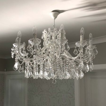 A crystal chandelier with ornate detailing and multiple candle-shaped bulbs hangs from a white ceiling, casting intricate shadows.