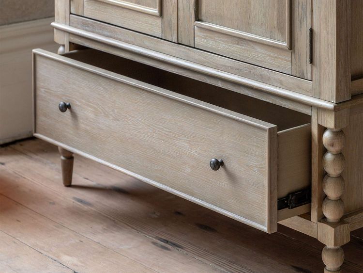 Wooden cabinet with an open lower drawer, featuring round knobs and decorative legs, on a wooden floor.