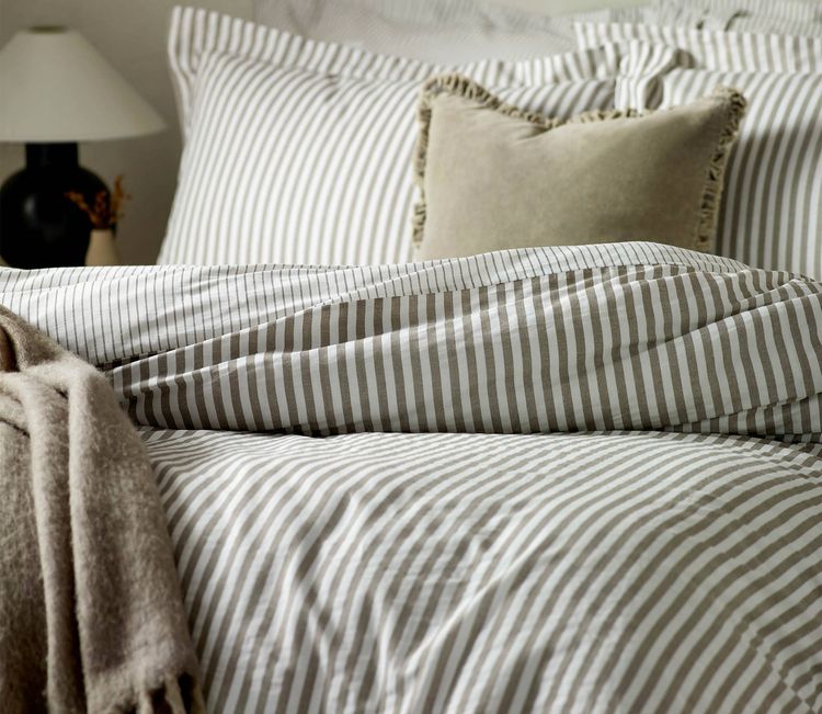 Cozy bed with striped bedding, a beige throw, and a decorative pillow. A lamp is visible in the background.