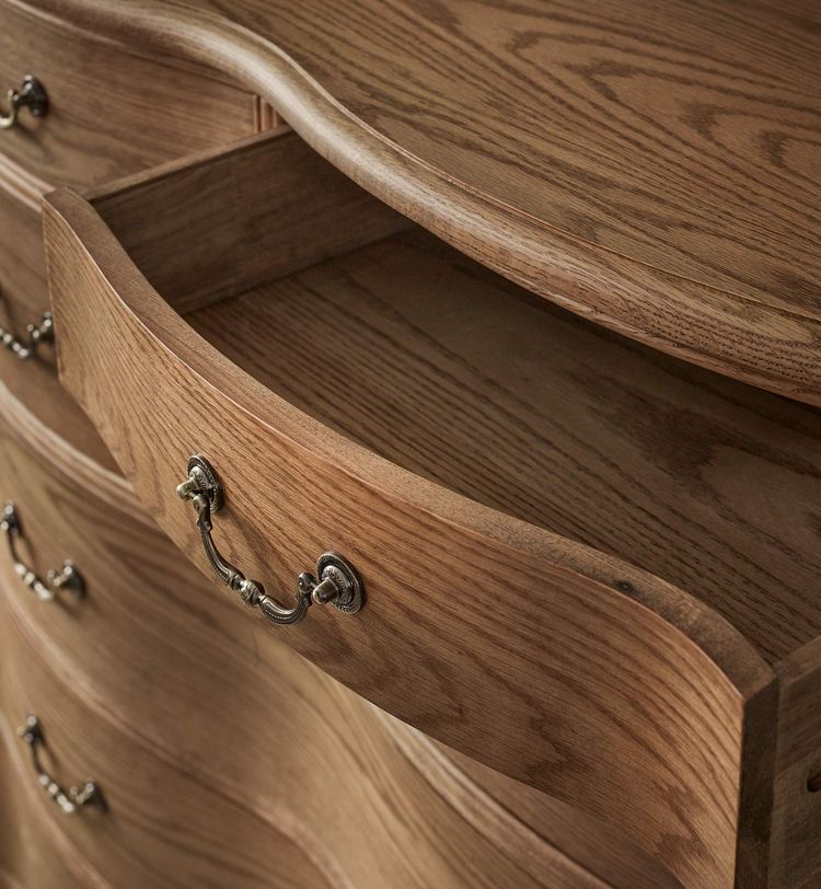 Open wooden dresser drawer with ornate metal handle, showing smooth grain and curved design.