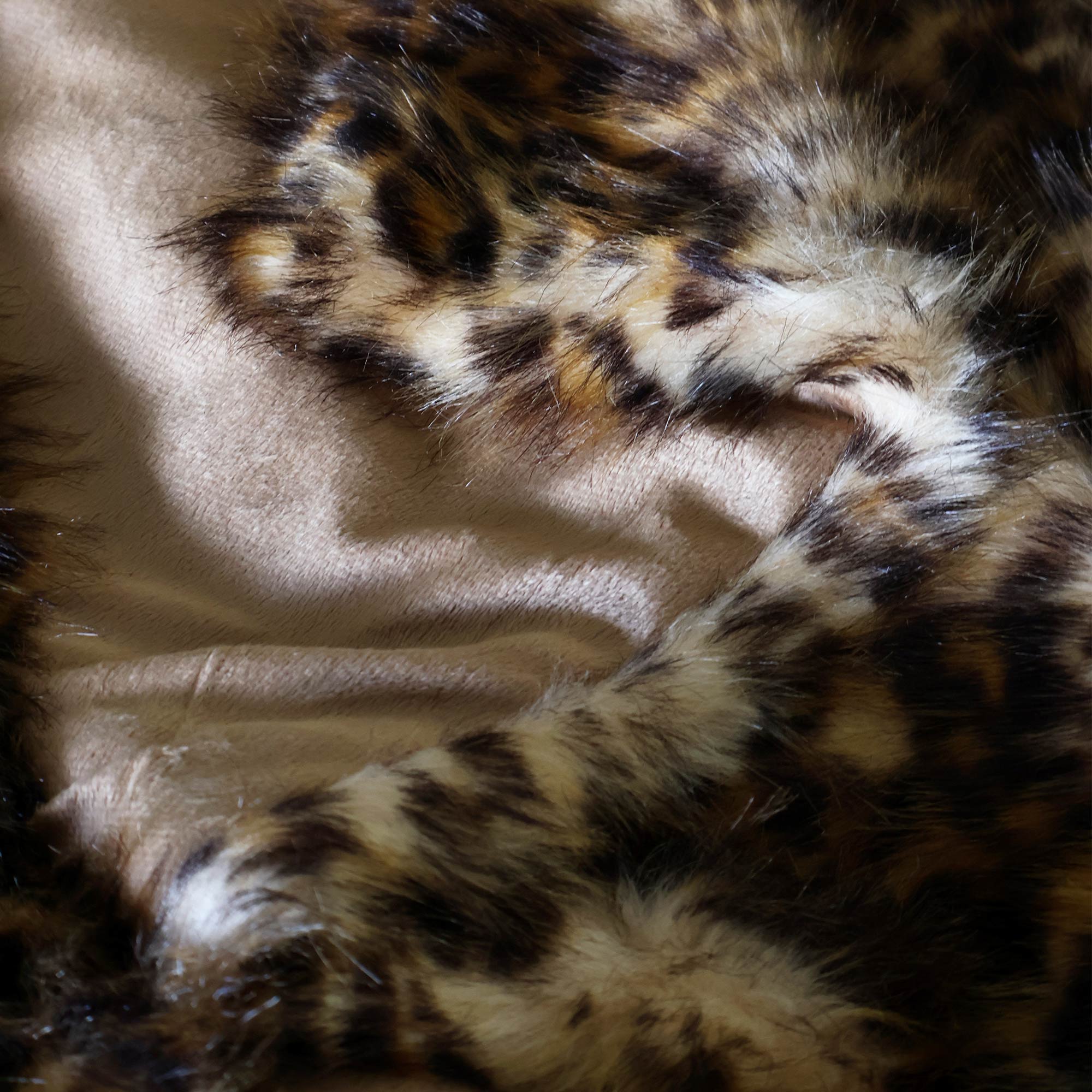 Close-up of a leopard print faux fur fabric with a soft beige lining, showing its texture and pattern in detail.