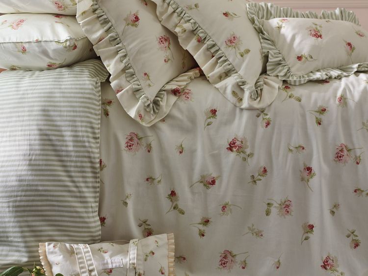 Floral and striped bedding with ruffled edges on a neatly made bed, featuring pink roses and green leaves.