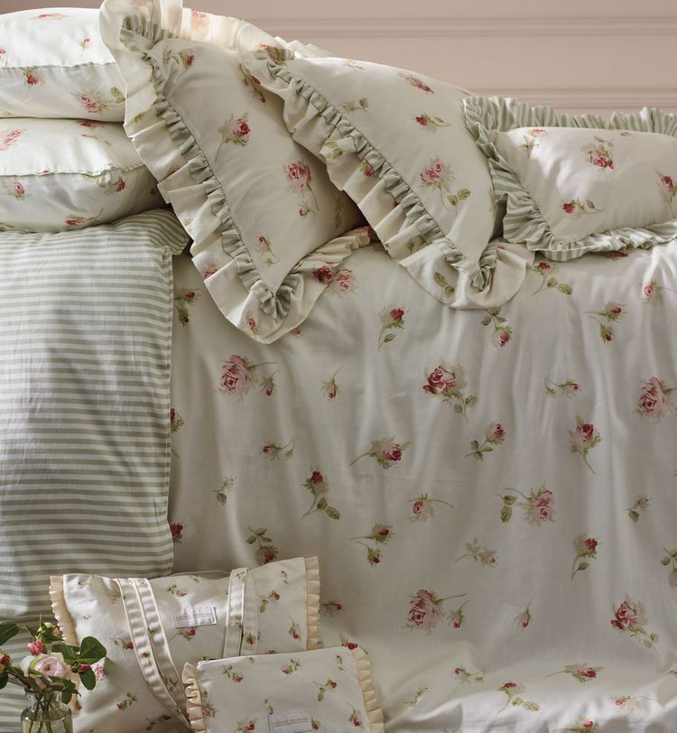 Floral and striped bedding with ruffled edges on a neatly made bed, featuring pink roses and green leaves.