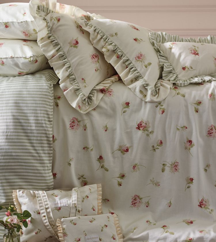 Floral and striped bedding with ruffled edges on a neatly made bed, featuring pink roses and green leaves.