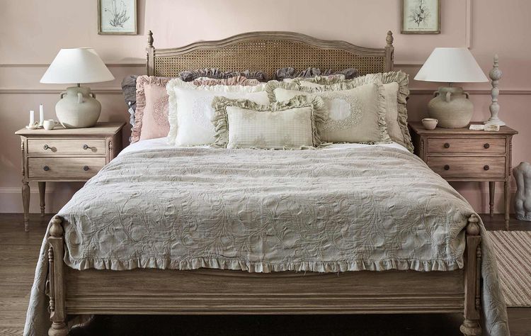 Cozy bedroom with a wooden bed, layered pillows, two bedside tables with lamps, and soft pink walls adorned with framed art.