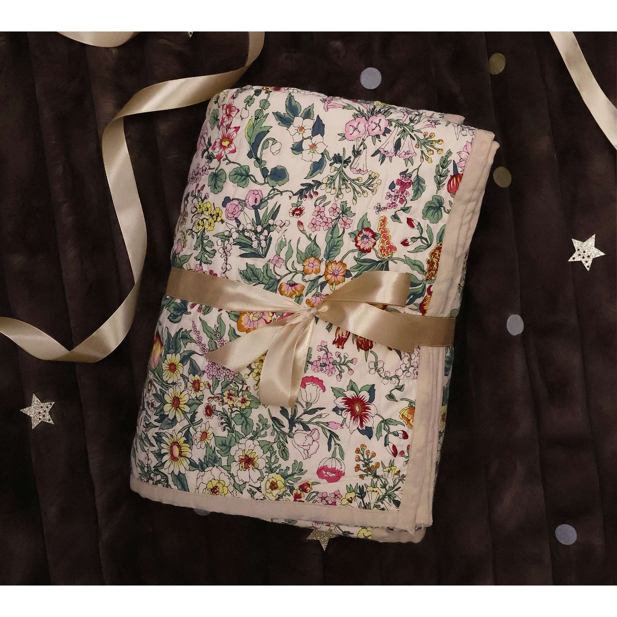 A floral-patterned blanket tied with a satin ribbon rests on a dark, star-patterned quilt.