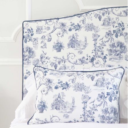 Blue and white floral-patterned pillow and headboard with intricate designs, set against a white wall.