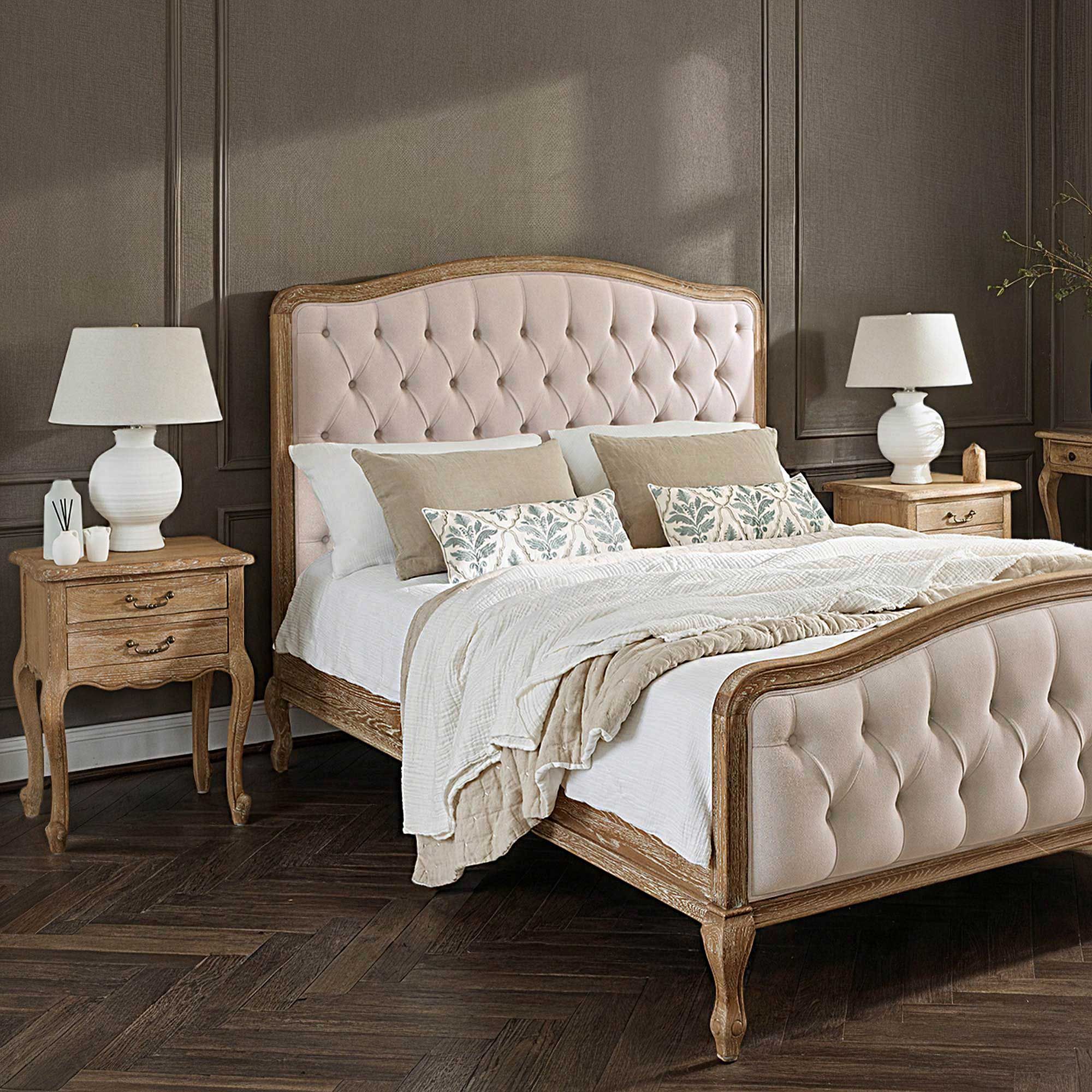 Elegant bedroom with a tufted bed, white bedding, two wooden nightstands with lamps, and a herringbone wood floor.