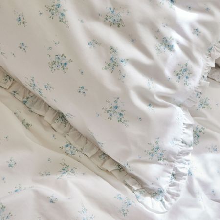 White bed linen with small blue floral patterns and ruffled edges.