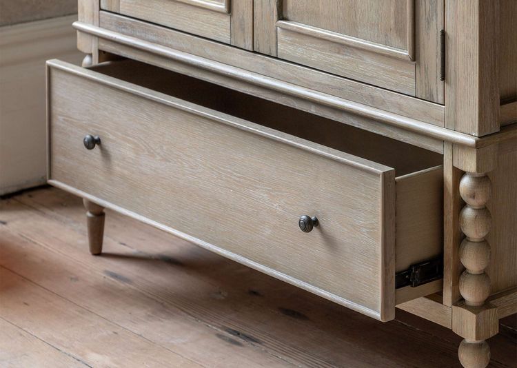 Wooden cabinet with an open drawer at the bottom, featuring round handles, stands on a hardwood floor.