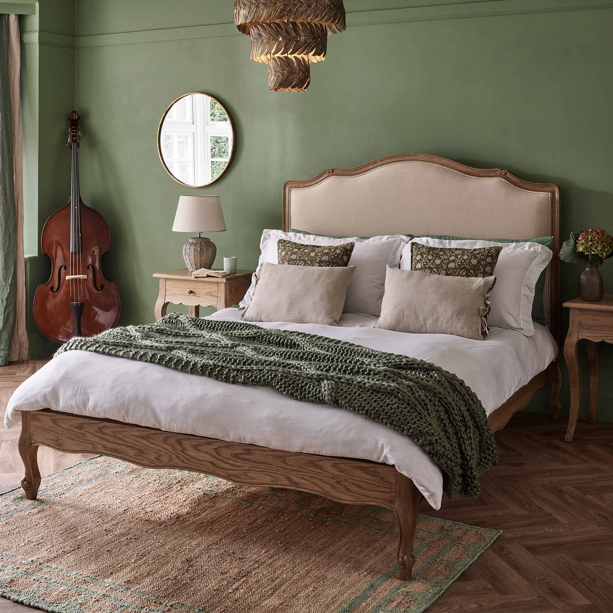 Cozy bedroom with a wooden bed, green walls, a knitted throw, and a double bass in the corner. Warm, earthy tones create a relaxing atmosphere.