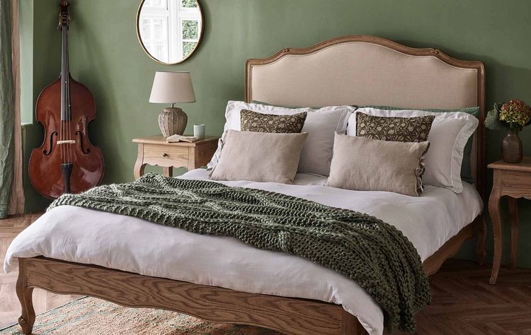 Cozy bedroom with a wooden bed, green walls, a knitted throw, and a double bass in the corner. Warm, earthy tones create a relaxing atmosphere.