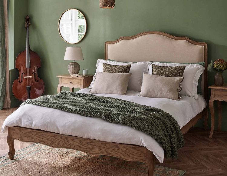 Cozy bedroom with a wooden bed, green walls, a knitted throw, and a double bass in the corner. Warm, earthy tones create a relaxing atmosphere.