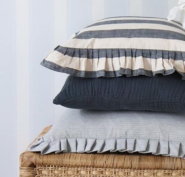 Three stacked pillows with ruffled edges: top pillow has gray and white stripes, middle is solid dark gray, bottom is light gray.