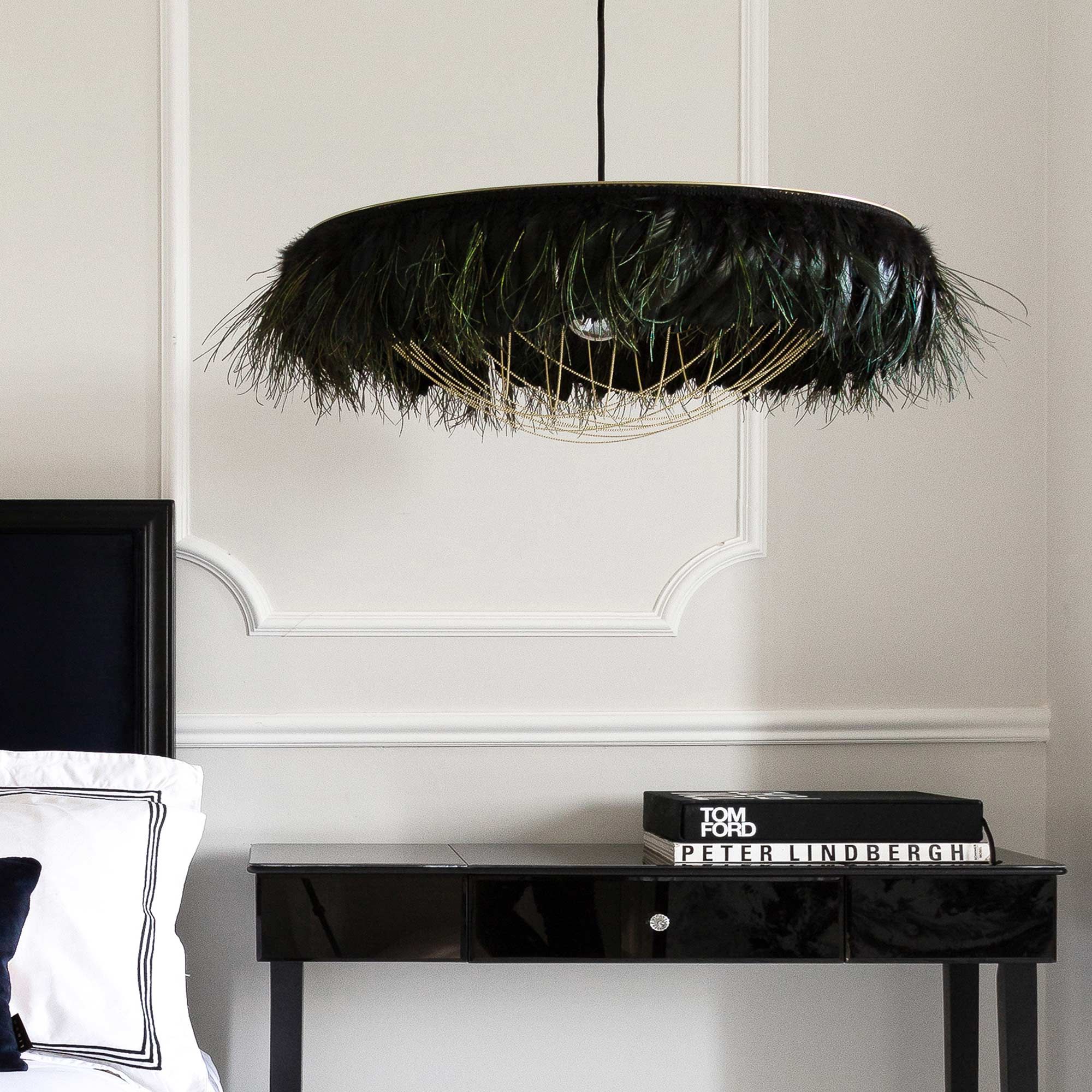 Elegant room with a black feathered chandelier, white paneled wall, black headboard, and glossy black side table with stacked books.