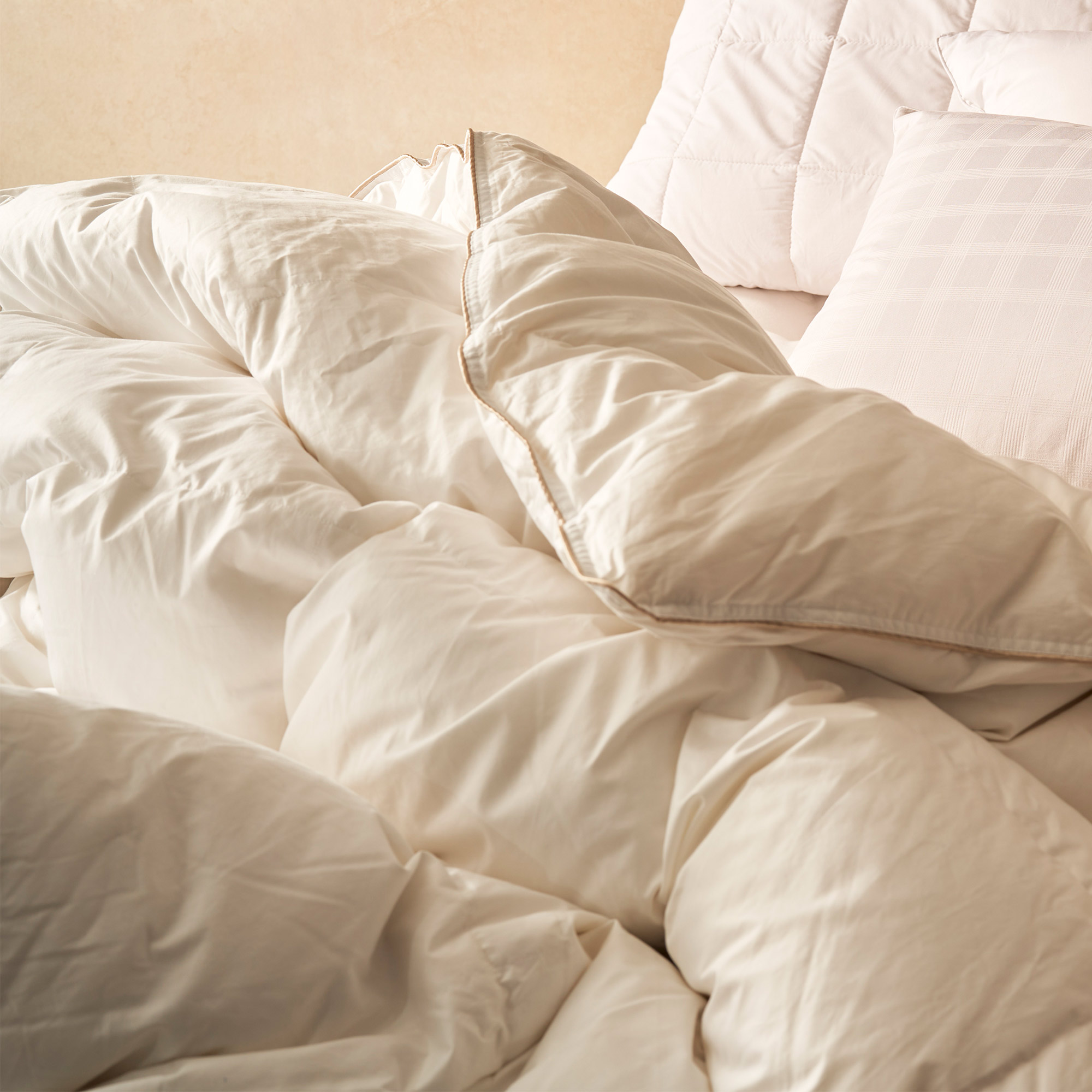 A cosy, rumpled bed with cream-colored sheets, pillows, and a comforter, creating a warm and inviting atmosphere.