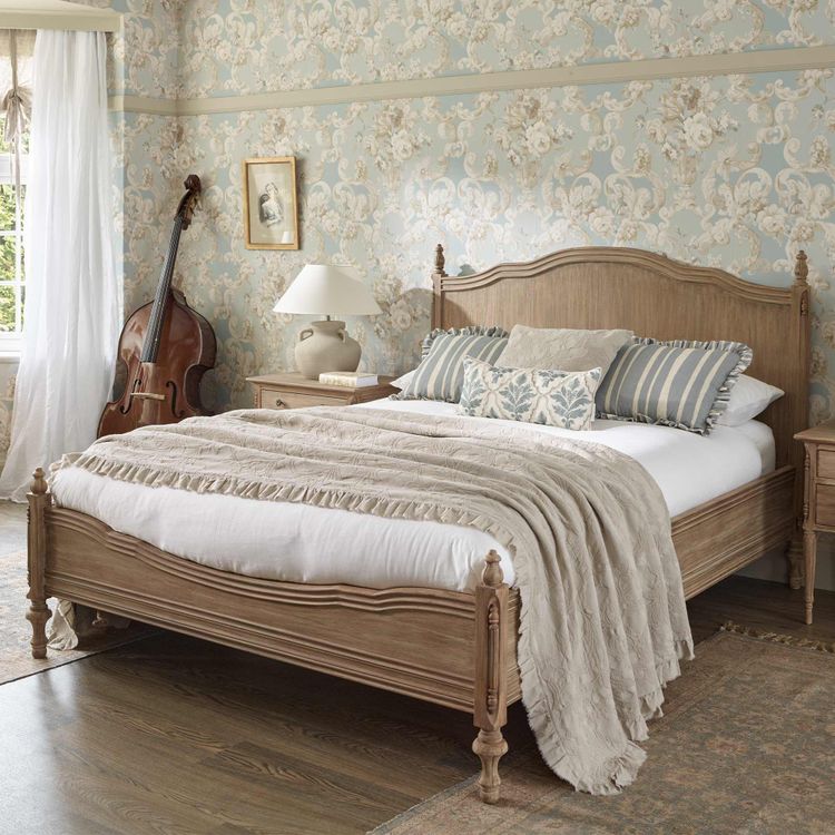 Elegant bedroom with a wooden bed, patterned pillows, floral wallpaper, a double bass in the corner, and a window with sheer curtains.