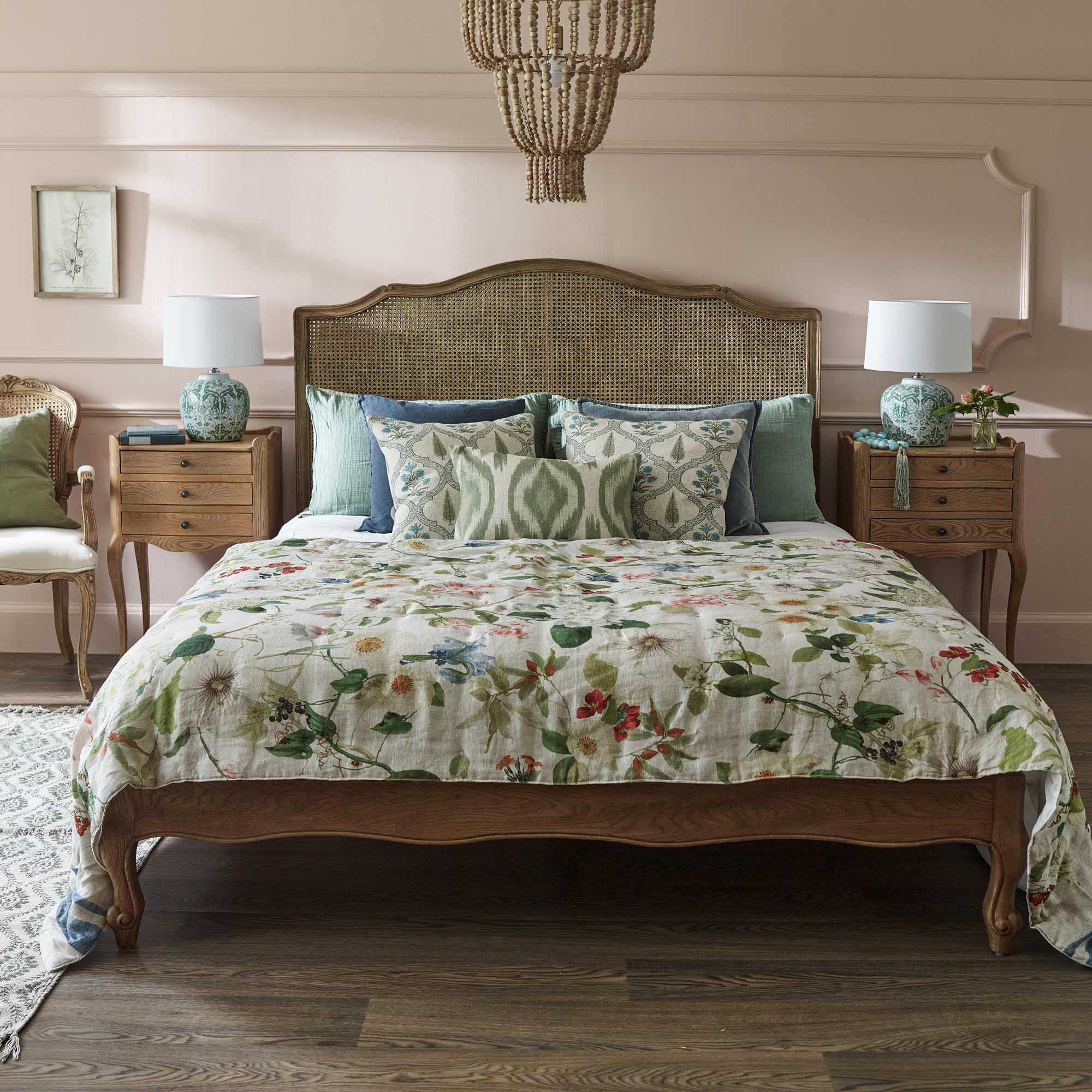 Cozy bedroom with a floral bedspread, wooden bed frame, patterned pillows, wooden nightstands, lamps, and a woven chandelier.