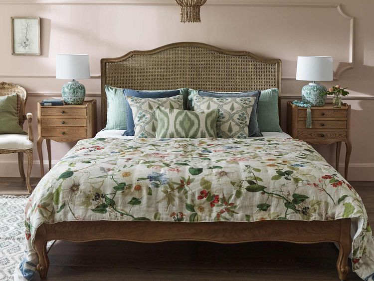 Cozy bedroom with a floral bedspread, wooden bed frame, patterned pillows, wooden nightstands, lamps, and a woven chandelier.