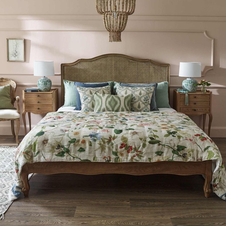 Cozy bedroom with a floral bedspread, wooden bed frame, patterned pillows, wooden nightstands, lamps, and a woven chandelier.