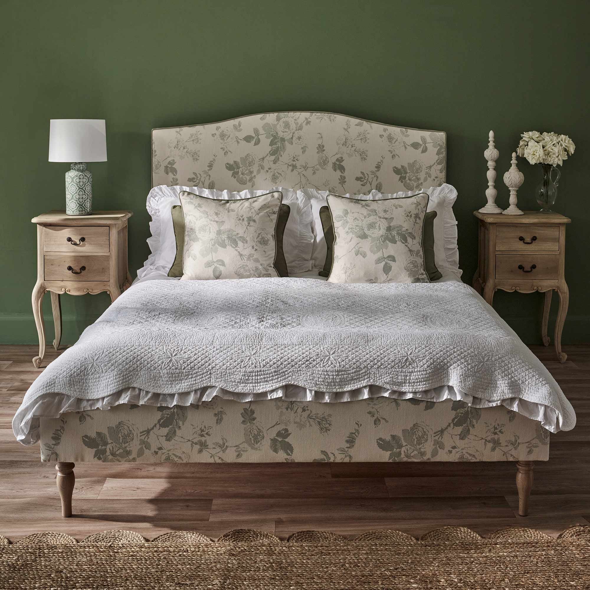 Elegant bedroom with a floral-patterned bed, white bedding, green accent pillows, wooden side tables, and a green wall.