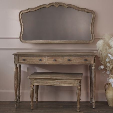 Vintage wooden vanity set with an ornate mirror, three drawers, and a matching bench. The set is placed against a soft pink wall.