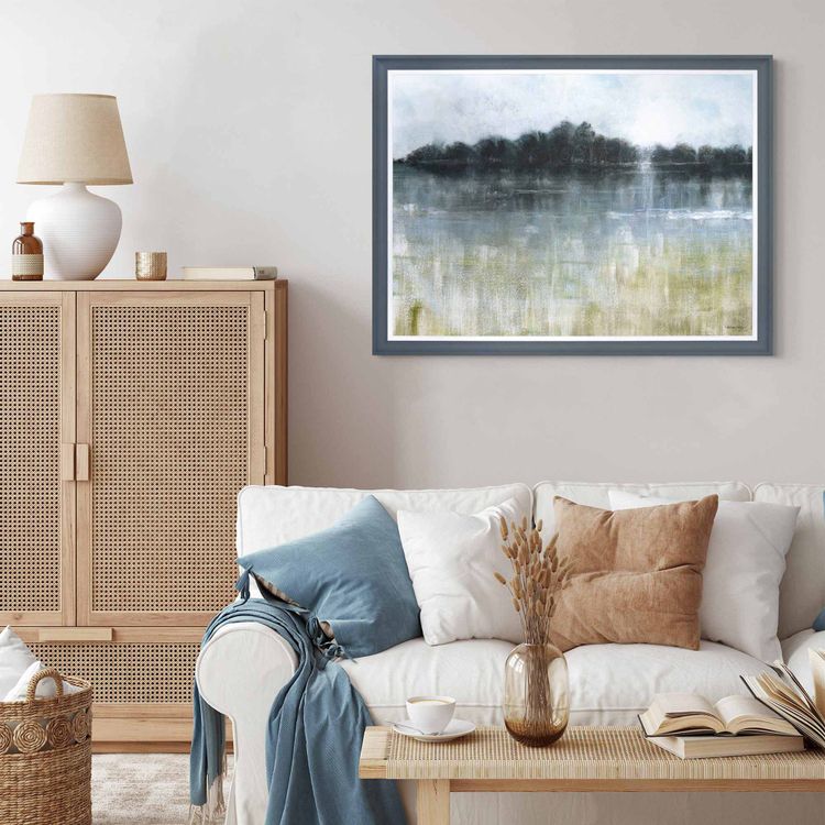A cosy living room with a white sofa, blue and beige cushions, a wooden cabinet, and a landscape painting on the wall.