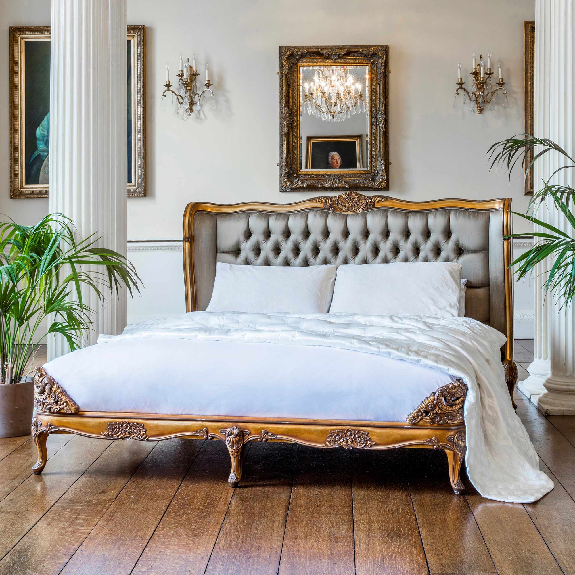 Elegant bedroom with a tufted headboard, ornate wooden bed frame, white bedding, and classic decor including chandeliers and framed paintings.