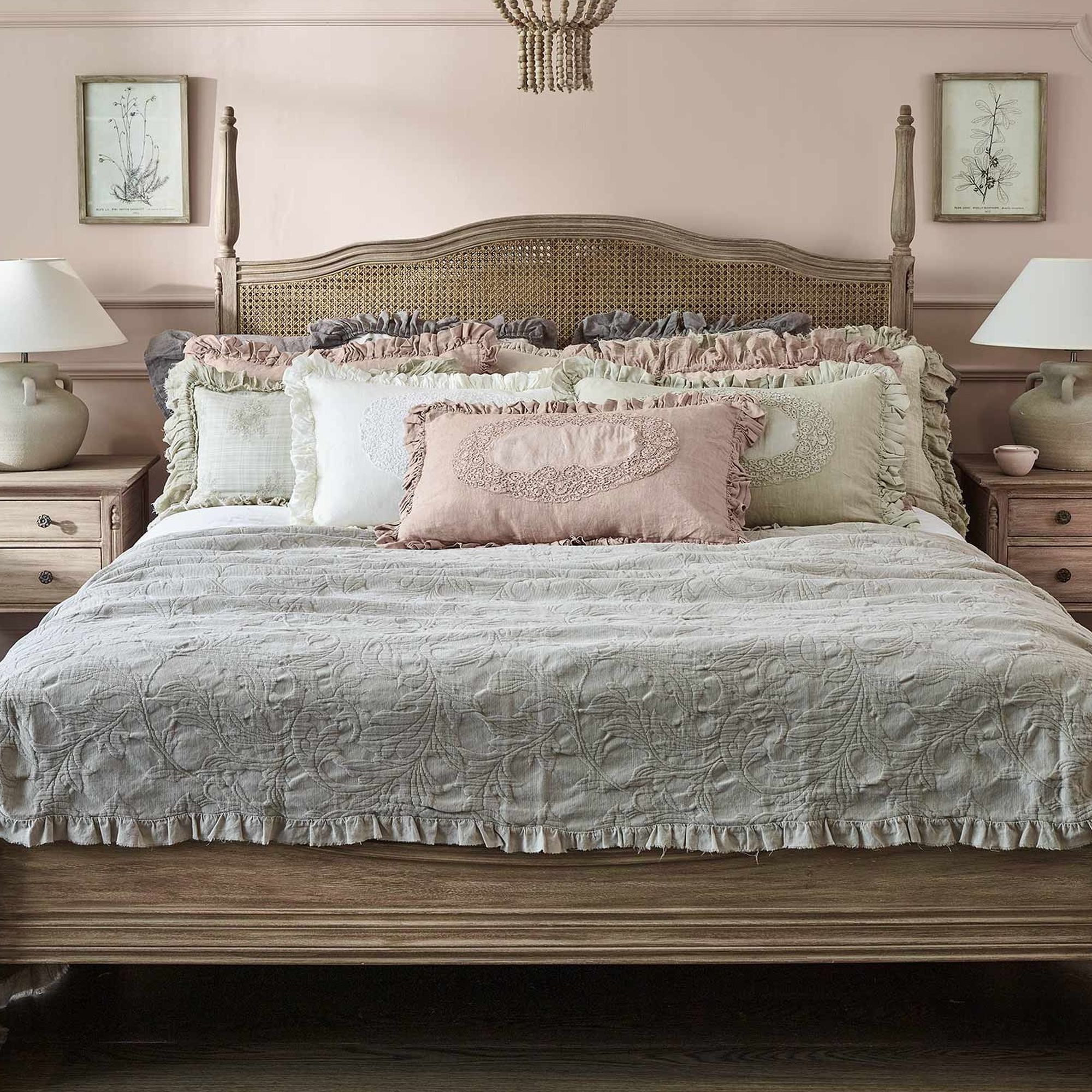 Cozy bedroom with a wooden bed, pastel pink and beige bedding, two bedside tables, and table lamps against a soft pink wall.