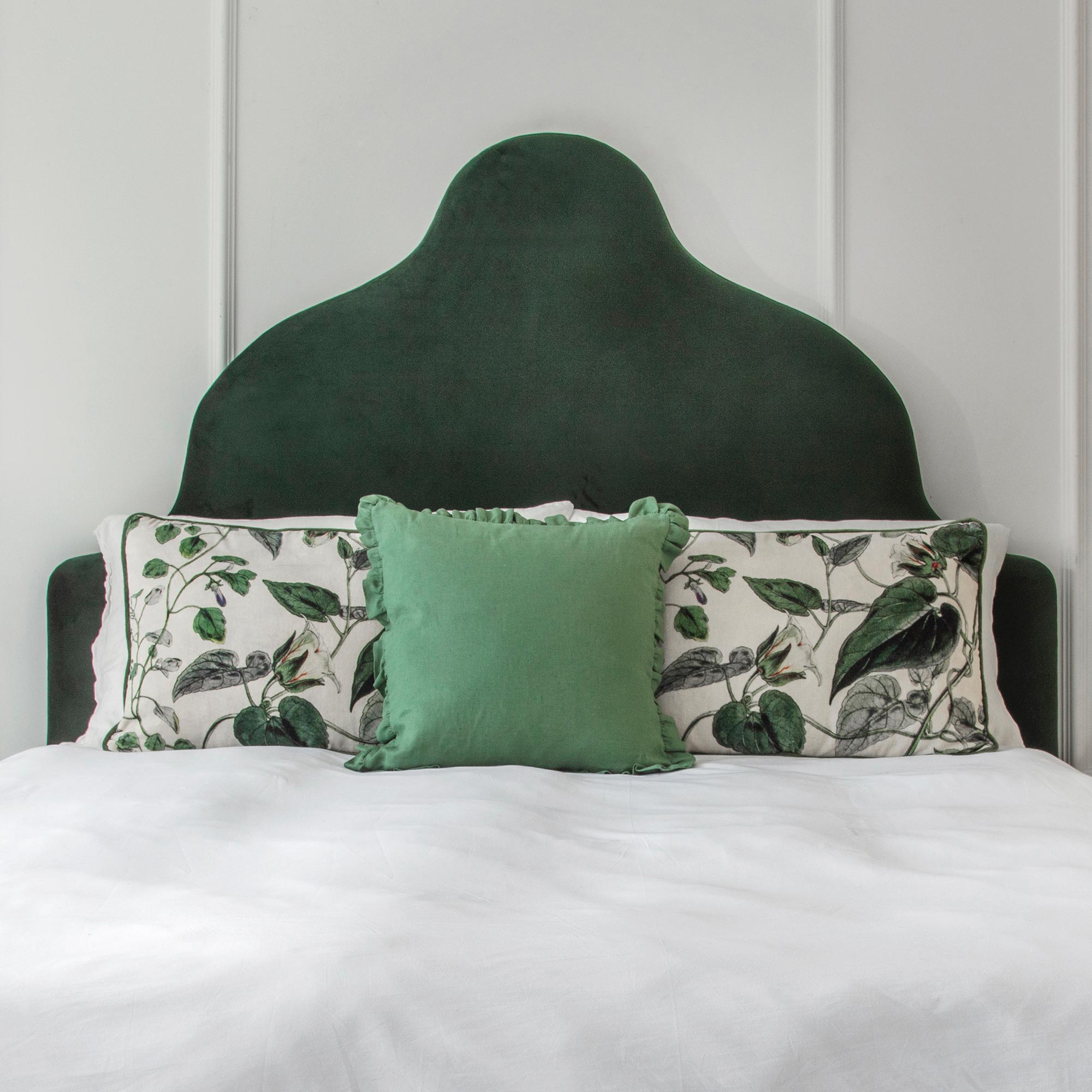 Elegant bed with a dark green velvet headboard, floral-patterned pillows, and a plain green cushion on a white duvet.
