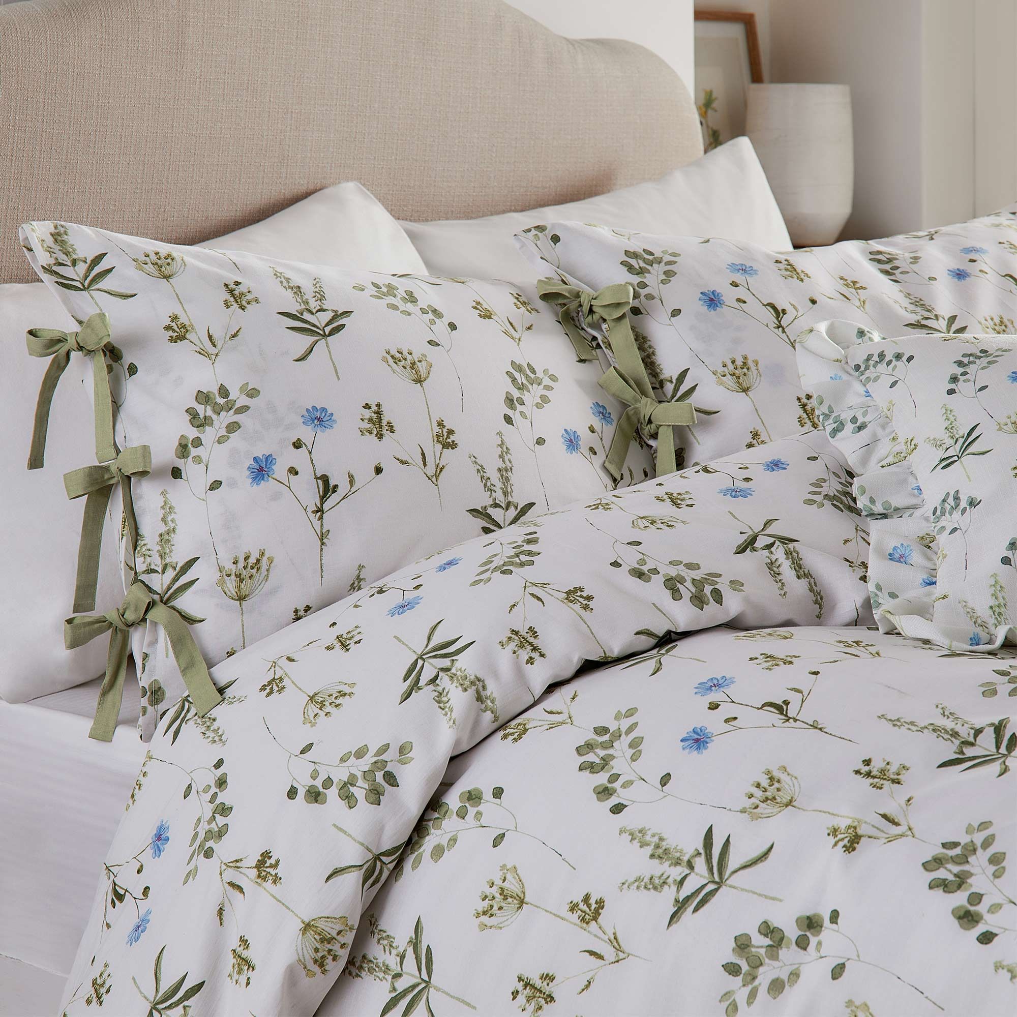 Floral-patterned bedding with green and blue flowers, featuring decorative green ribbon ties, on a neatly made bed with a beige headboard.