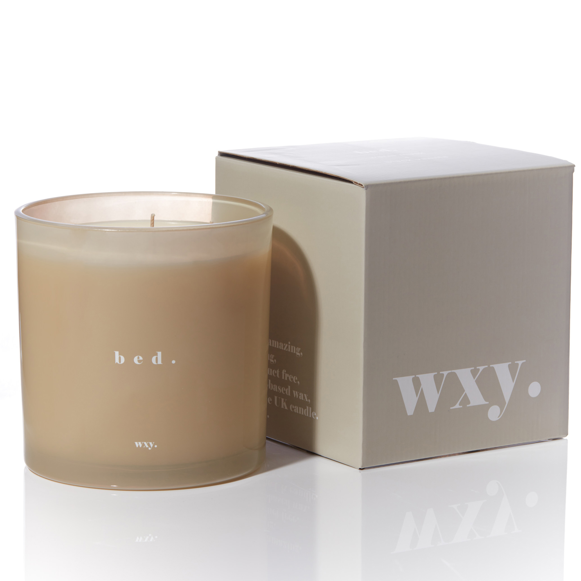 A beige candle in a glass holder labeled "bed." next to its box, which has "WXY." printed on it.