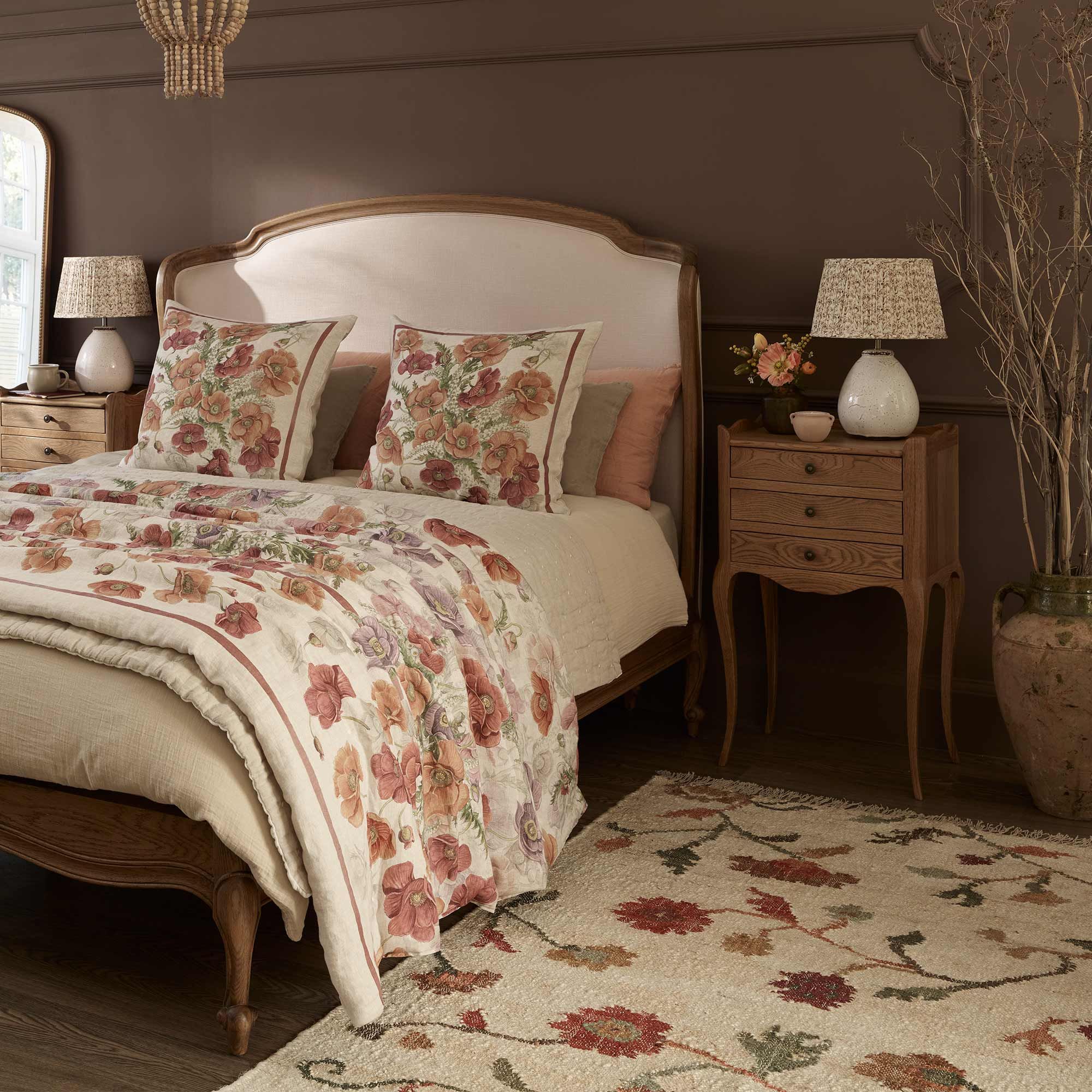 Cozy bedroom with a floral-themed bedspread, matching pillows, wooden furniture, and a patterned rug on a dark wood floor.