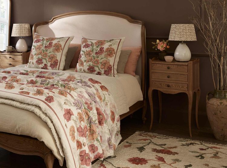 Cozy bedroom with a floral-themed bedspread, matching pillows, wooden furniture, and a patterned rug on a dark wood floor.
