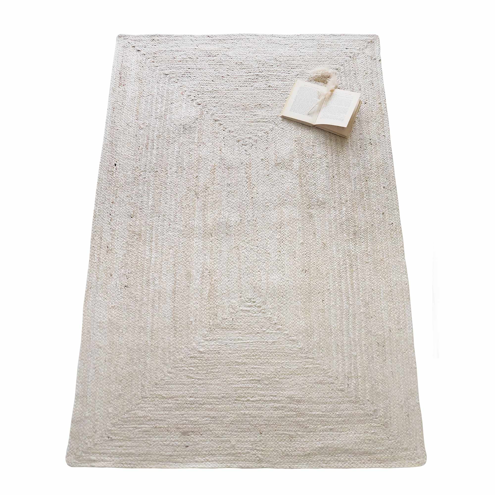 A textured beige rectangular rug with a book and tassel bookmark placed on the top right corner.