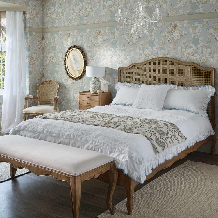 Elegant bedroom with a vintage feel, featuring a wooden rattan bed, chandelier, and natural light from a large window.